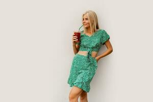 Pretty blond woman in stylish  spring dress holding tasty lemonade and posing over white background. photo