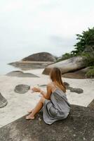 elegante mujer en gris seda vestir posando en solitario playa en nublado clima. ver desde atrás. foto