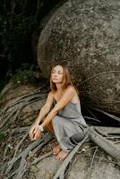 elegante morena mujer en seda gris vestir posando en en el rocas foto