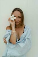 Stylish  brunette woman  in beautiful  blue playsuit  holding flower and posing over white wall. photo