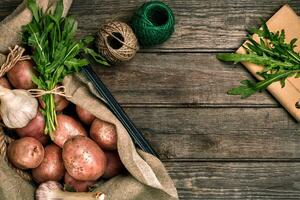 Raw whole washed organic potatoes, garlic and ruccola on sackcloth over old wooden plank background. Top view with space. Close up photo