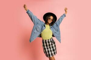 Ecstatic laughing   woman in black hat and jeans jacket having fun  on pink background in studio. photo