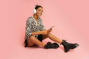 Ecstatic woman  with pleasue listening lovely music  on pink background.  Holding mobyle phone. Wearing stylish blouse and leather skirt. photo