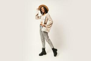 Fashion studio  photo of stylish smiling woman  in casual outfit posing on white background. Wearing beige hat and jeans.  Full lenght.