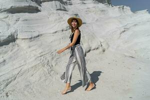 de viaje mujer en Paja sombrero caminando terminado blanco Roca paisaje en delkikli koy en Egeo mar. lleno largo. foto