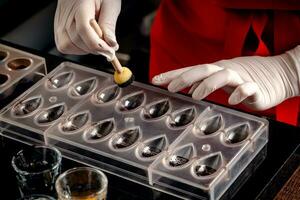 A woman confectioner with red uniform and white sterile gloves do a set of colorful chocolates from milk chocolate on a table. photo