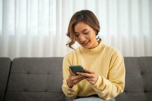 woman sitting on a sofa using a mobile phone, Happy relaxed smiling lady laughing holding smartphone, looking at cellphone enjoying doing online e-commerce shopping in mobile apps or watching videos. photo