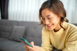 woman sitting on a sofa using a mobile phone, Happy relaxed smiling lady laughing holding smartphone, looking at cellphone enjoying doing online e-commerce shopping in mobile apps or watching videos. photo