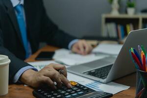 Businessman working on desk with calculator and document data with laptop computer. Business financial money account and tax fee concept. photo