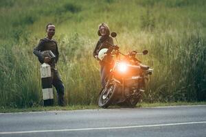 asian couple holding safety helmet standing beside small enduro motorcycle against beautiful green grass photo