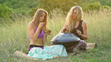 Young girls play and sing on the musical instrument Handpan. Practice meditation at sunset video