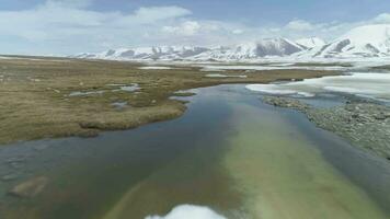 schnell fliegend Über klein Seen mit Eis Blöcke im Frühling. schneebedeckt Berge auf Hintergrund. Antenne niedrig Winkel Sicht. Arabel Plateau. Kirgisistan video