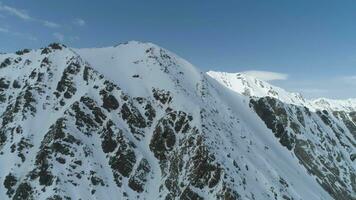 Flying Sideways and Upward near Snowy Mountain Peaks at Sunny Day. Aerial View. Establishing Shot video