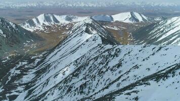 nevoso montagne a soleggiato giorno. aereo Visualizza. fuco è volante inoltrare al di sopra di montagna cresta. telecamera è ribaltamento su. stabilendo tiro a alto altitudine video