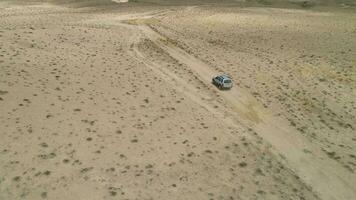 suv carro vai em arenoso terreno baldio. deserto panorama e lago costa em fundo. aéreo visualizar. zangão é órbita em volta. estabelecendo tiro video