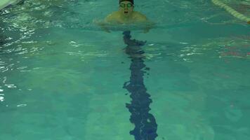 atletisch Kaukasisch Mens met pet en stofbril is zwemmen schoolslag stijl in zwembad met blauw water naar de camera. langzaam beweging. video