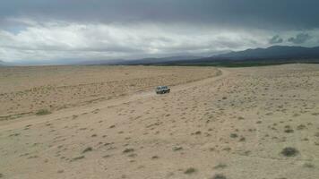 Suv Car Goes on Sandy Wasteland. Desert Landscape and Stormy Clouds. Aerial Low Angle View. Drone is Flying Sideways and Distancing From Car video