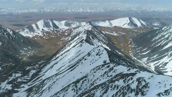neigeux montagnes à ensoleillé journée. aérien voir. drone est en volant en arrière plus de Montagne crête. caméra est basculant en haut. établissement coup à haute altitude video
