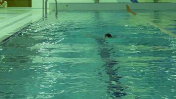 atlético caucásico hombre con gorra y gafas de protección es nadando braza de pecho en piscina con azul agua. video