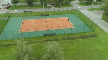 spelare är spelar tennis på domstol i grön urban parkera. antenn vertikal topp se. Drönare är flygande runt om. avlägsen skott. video