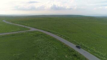 Minivan car is going on asphalt road. Green meadow, grey sky with clouds. Aerial view, drone flying forward. video