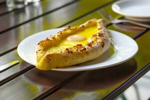 estilo adjara khachapuri, horneado masa con huevo, queso y dos piezas de mantequilla en un blanco plato en un cafetería. foto