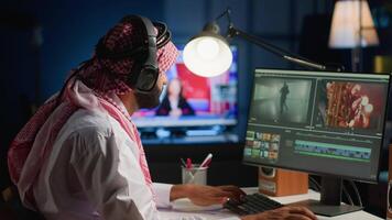 Muslim cinematographer wearing headphones while editing project, creating film montage, working with images and sounds. Man using video cutting software to process movie on PC workstation