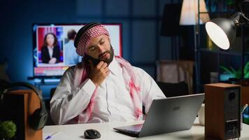 Arabo lavoratore segreteria Telefono chiamata mentre remoto Lavorando a partire dal accogliente casa ufficio. telelavoratore parlando con collega utilizzando smartphone, discutere lavoro d'ufficio e compiti bisognoso per essere risolto video