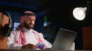 Happy arab man doing internet shopping on computer, spneding money on frivolous things. Smiling Middle Eastern person adding payment method on website in order to purchase products video