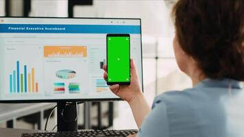 Businesswoman holding greenscreen on phone and working on marketing development at agency office desk. Company employee using mockup chromakey template and isolated copyspace on display. video