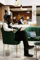 Focused concentrated hotel manager holding digital tablet using front desk software, confirming online bookings while sitting in lobby. Innovative technologies in hospitality industry photo