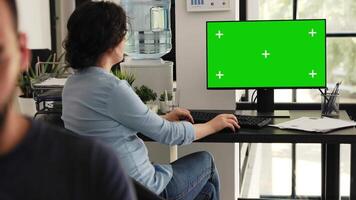 Office employee looks at greenscreen sitting at workstation, checking isolated chromakey display on computer monitor. Woman typing information and examining blank mockup desktop. video