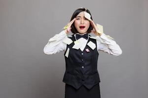 Stressed asian waitress overloaded with tasks sticky notes holding hands on head portrait. Frustrated woman receptionist in uniform with burnout and workload looking at camera photo