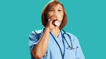 Satisfied BIPOC healthcare expert enjoying fresh cup of coffee during job shift break. Happy certified nurse isolated over studio background drinking hot beverage, close up photo