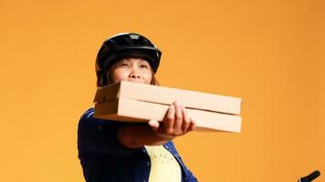 Hip level close up shot of cheerful courier looking at camera, showing approval gesture while delivering takeout meals. Friendly cyclist offering pizza to customer, isolated over studio background photo