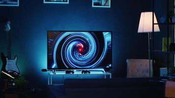 Zoom in shot on TV screen showing 3D render animations in empty stylish neon lit home studio interior. Modern apartment illuminated with RGB lights at night and artwork decorating the walls video