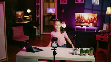 Energetic young girl filming herself discussing topics of interest for children watching her online social media content. Happy little influencer recording video targeting gen Z viewers, jib down shot