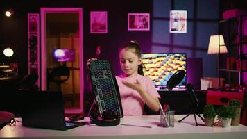 Kid influencer in studio using camera to review gaming keyboard, mouse and headphones. Child show host filming electronics haul, presenting wired computer peripherals to viewers video