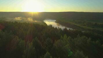 Drone is flying forward over the tops of trees and river at misty sunrise. Aerial view. video