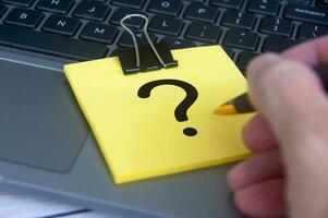 Question mark on yellow notepad with laptop background. Question and Answer session. photo