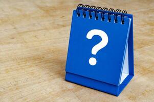 Question mark on blue notepad on wooden background. Question and answer session. photo