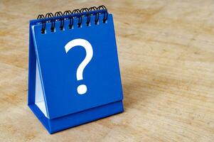 Close up of question mark on blue notepad on wooden background. Question and answer session photo