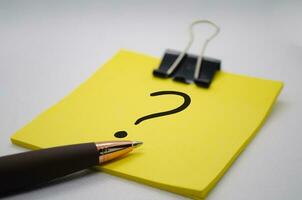 Close up of question mark on notepad with pen on white background. Question and answer concept. photo