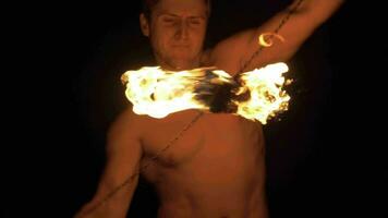 Man with muscular body is rotating two fireballs on chains. Super slow motion. video