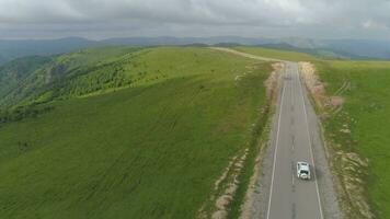 blanc suv voiture est Aller sur campagne asphalte route. vert collines et prairie, ciel avec des nuages. aérien voir. video
