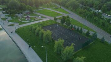 volante in giro Giocatori giocando tennis su un' Tribunale nel verde città parco. persone a piedi su marciapiede. aereo Visualizza. video