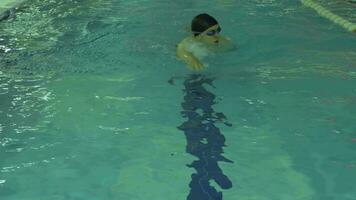 atlético caucásico hombre con gorra y gafas de protección es nadando gatear en piscina con azul agua hacia el cámara. lento movimiento. video