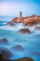 Ploumanac'h Lighthouse in Brittany, France. Long exposure sunset captures the turquoise water's serenity and the orange hue of the rocks on the Atlantic coast photo
