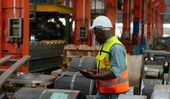Front view of young man worker using digital tablet to check stock in metal sheets storage of factory photo