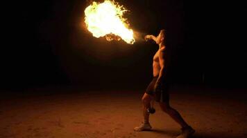 Muscular  young man is spraying kerosene on fire torch and erupting flame. Fire show. Slow motion video